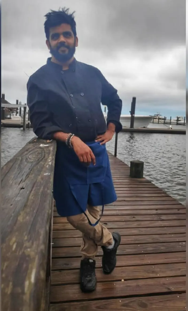 Chef Sanket in chef's whites on a wooden pier