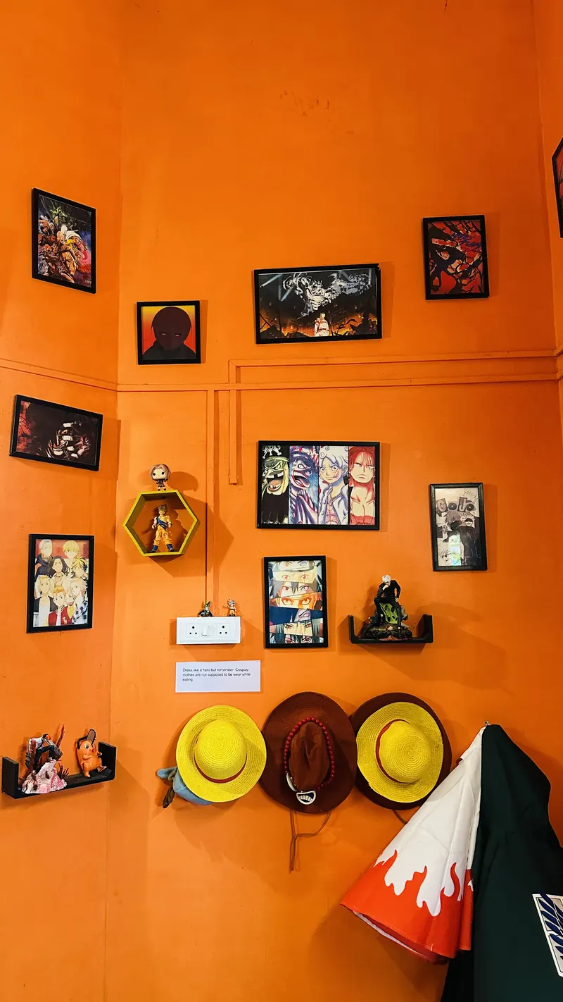 Orange wall with framed anime art and straw hats hanging on hooks